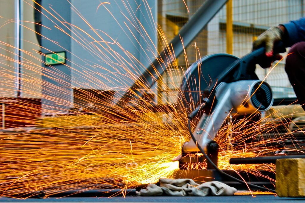 A worker operates a grinder cutting metal, creating a vibrant display of sparks in an industrial setting.