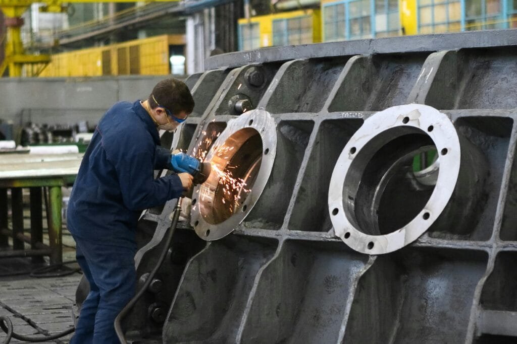 A worker in protective gear grinding metal, creating sparks in a factory setting.