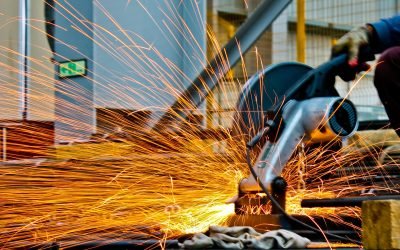 A worker operates a grinder cutting metal, creating a vibrant display of sparks in an industrial setting.