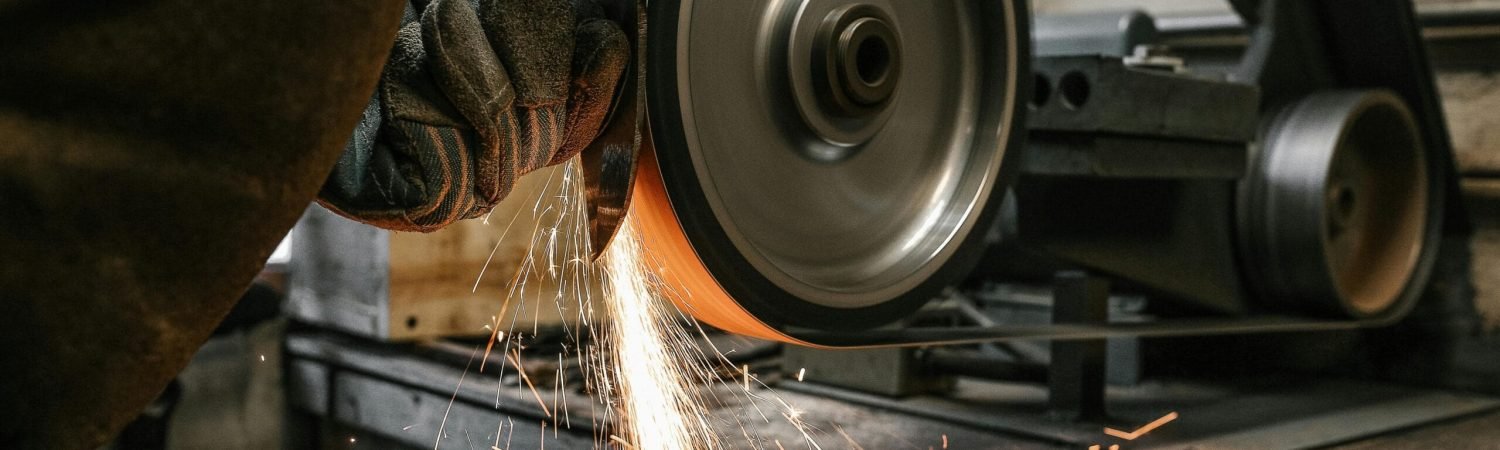 A close-up of a metalworker grinding a blade, creating sparks in a workshop setting.